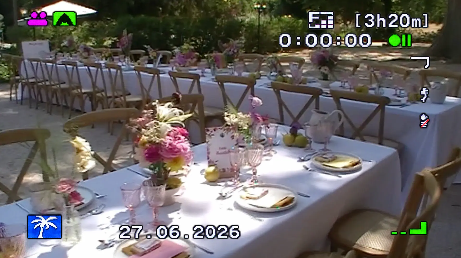 Tables de mariage en extérieur, décorées de fleurs roses, avec un affichage de caméscope vintage.