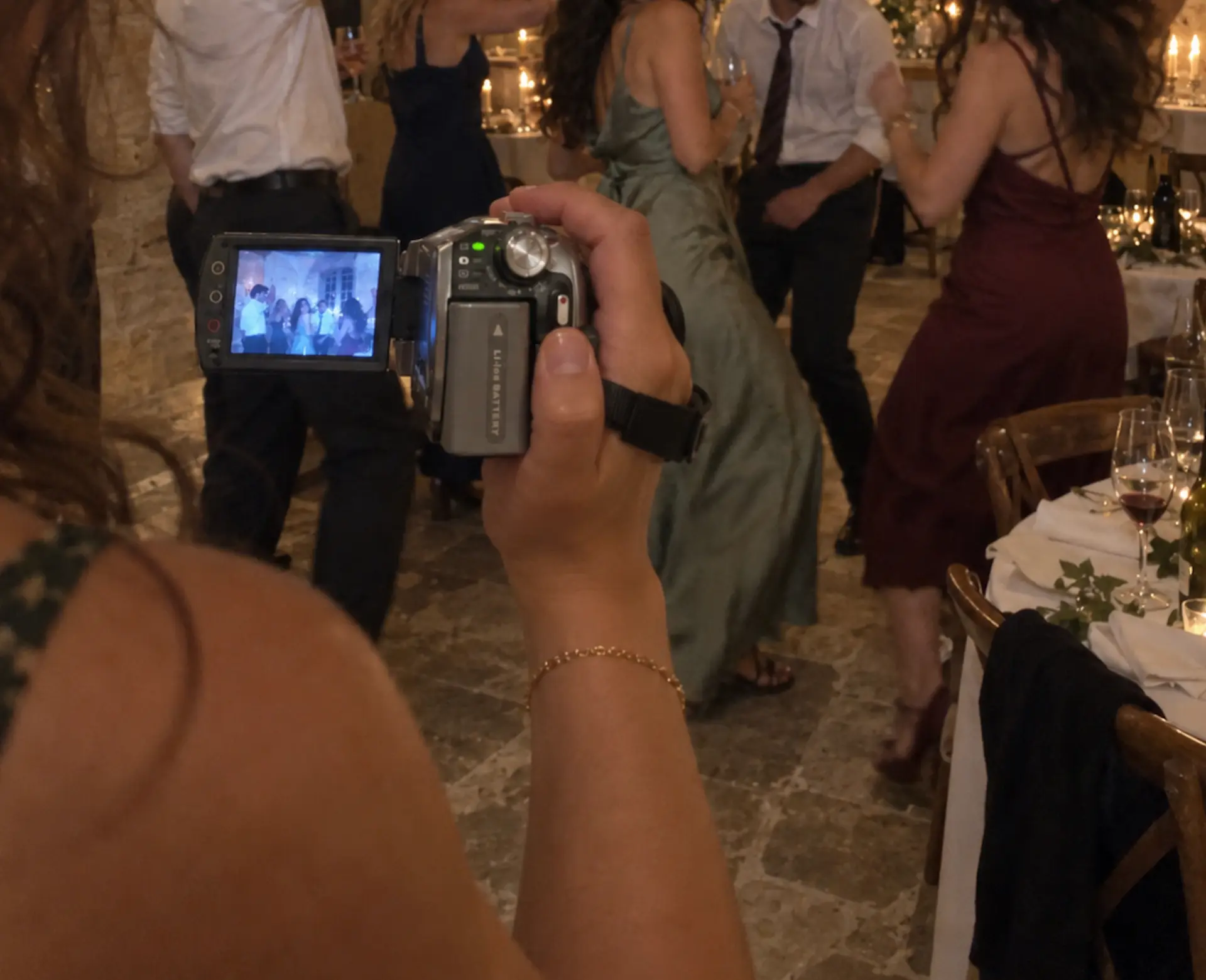 Une personne filme des invités avec un caméscope argenté dans une salle de réception en pierre.