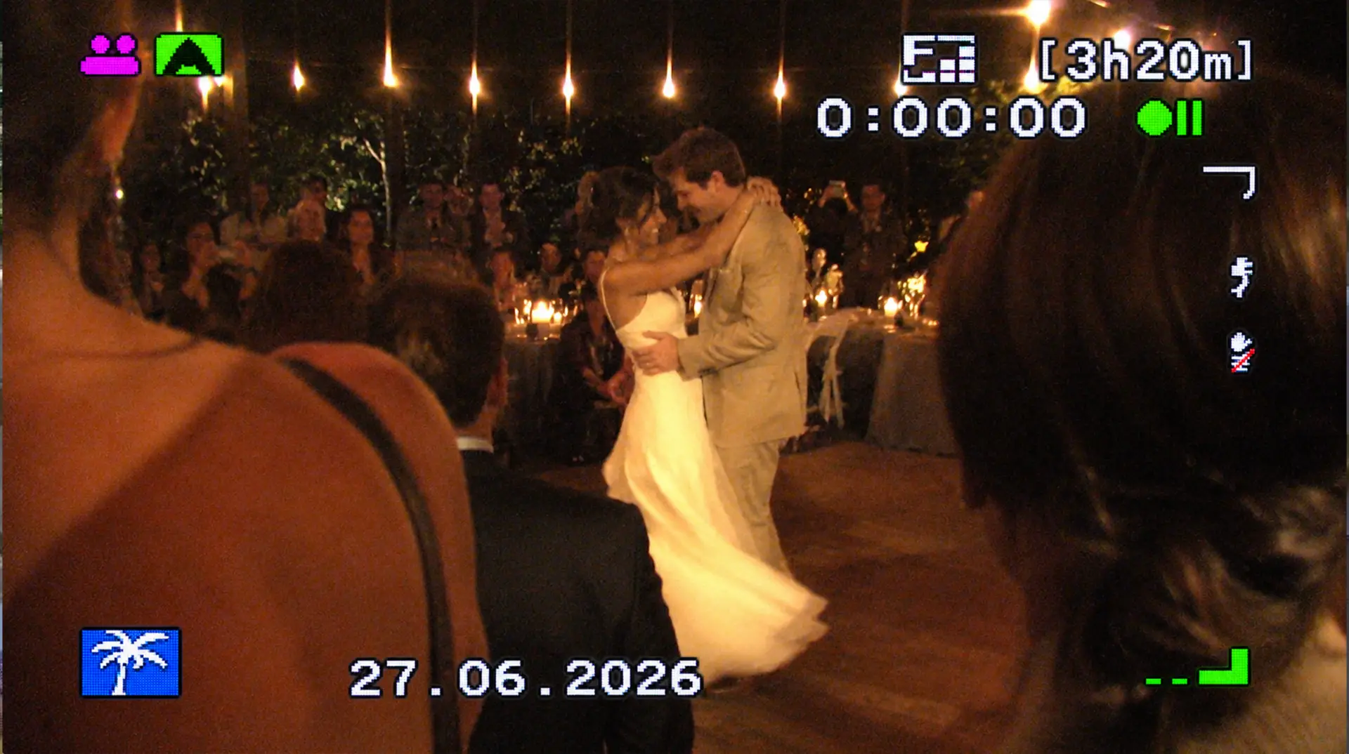Un couple de mariés danse au milieu des invités, sous des guirlandes lumineuses, avec un affichage de caméscope.